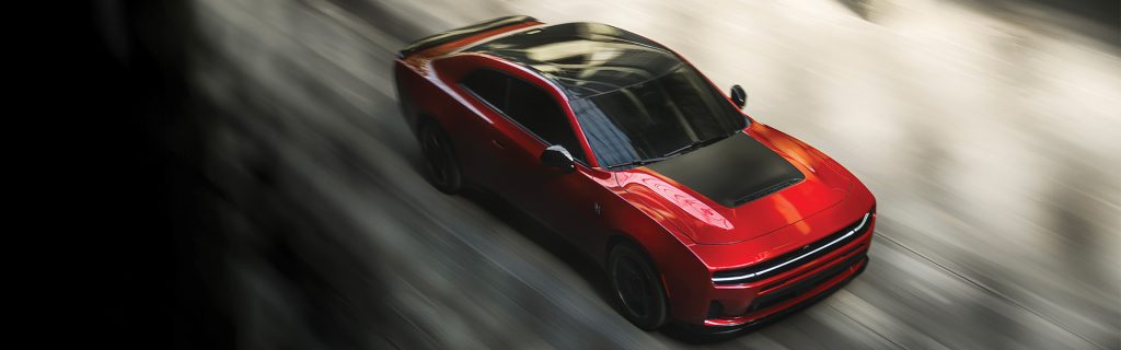 The image features a red Dodge Charger racing down a sleek urban road, emphasizing its high-performance design with a motion blur that highlights its speed and power.