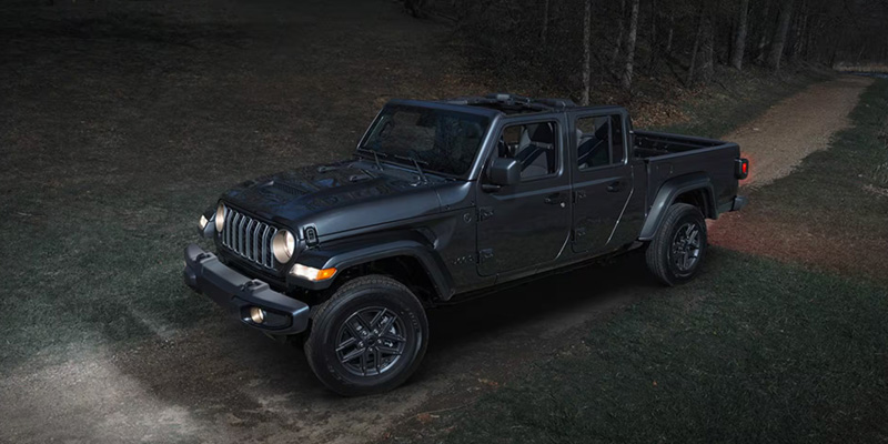 The image features a dark Jeep Gladiator, showcasing its rugged and versatile design, parked on a dirt path in a natural, off-road setting, ready for adventure.
