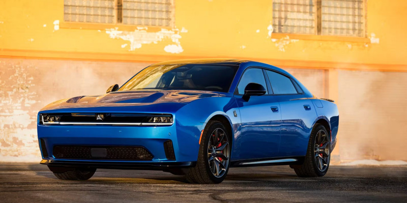 Blue Dodge Charger muscle car parked in front of an industrial-style building with a warm-toned backdrop.