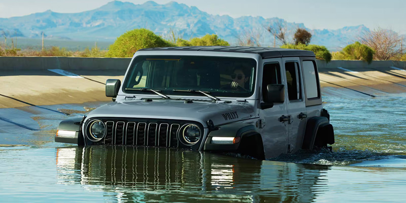 Silver Jeep Wrangler Willys driving through deep water.