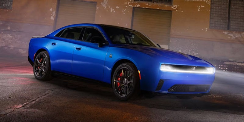 2026 Dodge Charger in vibrant blue, shown from a front three-quarter angle with illuminated LED headlights, black wheels, and red brake calipers.